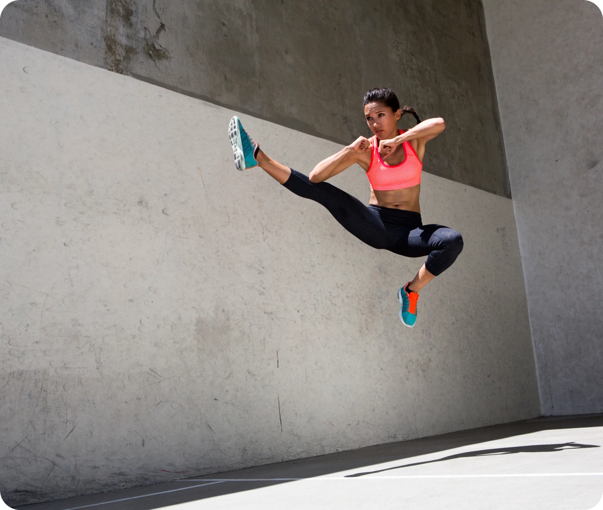 Athletic woman jumping against concrete wall